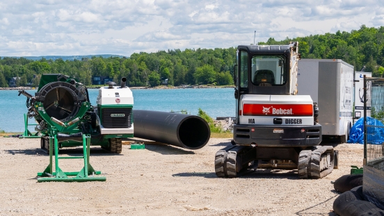 Pipe and fusing equipment staged on gravel laydown area with Bay in the background