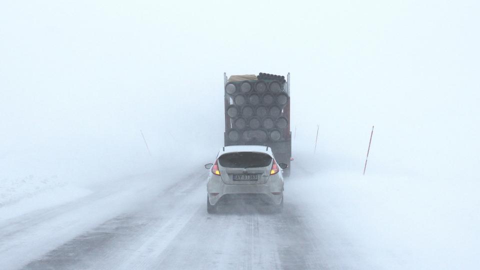 Car following transport truck on road during snow storm